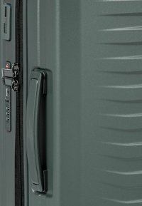 Valigia grigia con superficie testurizzata, chiusura a cerniera, lucchetto a combinazione e maniglia laterale per un facile trasporto.