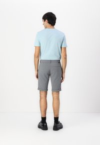 Lys blå t-skjorte med korte ermer paired med grå bomullsshorts, rullet kant, og svarte sko. Glatt tekstur og minimalistisk design.