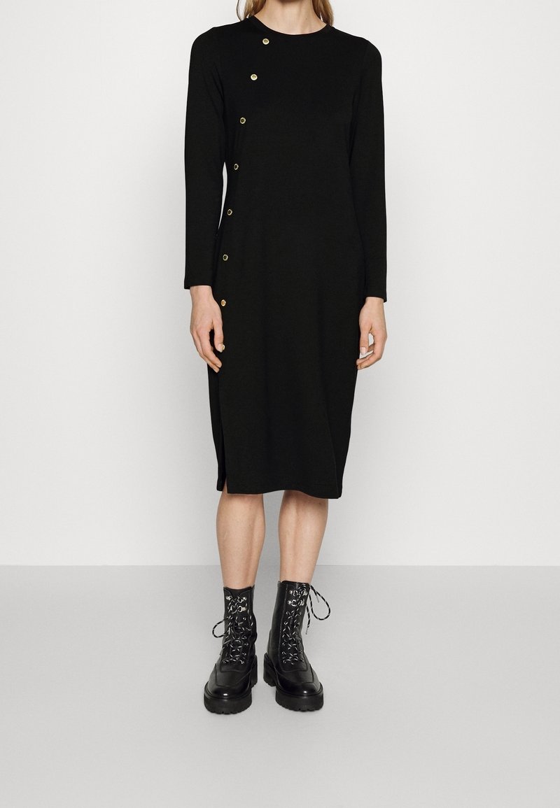 Černé dlouhé šaty s kulatým výstřihem, s akcenty zlatých knoflíků na boku a bočním rozparkem. V kombinaci s černými šněrovacími armádními botami.