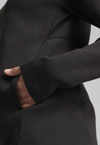Sudadera negra con una textura suave, diseño ajustado y bolsillo lateral. El puño tiene una costura reforzada para mayor durabilidad.