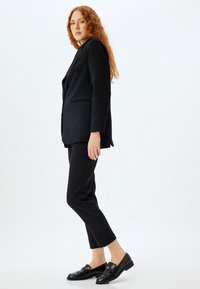 Blazer noir ajusté avec une coupe décontractée, associé à un pantalon noir slim et des mocassins noirs brillants. Tissu lisse avec des détails subtils.
