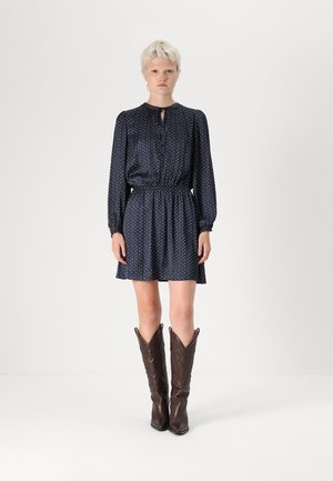 Abito blu navy con piccoli motivi multicolori, maniche lunghe e vita arricciata. Abbinato a stivali da cowboy marroni con un design decorativo.