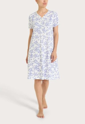 Donna che cammina a piedi nudi indossando un vestito bianco al ginocchio con maniche corte e un motivo floreale blu.