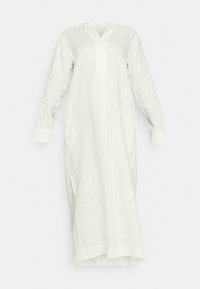 Longue robe blanche en lin avec manches longues, fente en V, fentes latérales et larges poignets, présentée sur un fond uni.