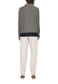 Blouse à rayures bleu marine et crème avec un col, des manches longues et un ourlet uni bleu marine ; associée à un pantalon crème et des talons beiges.