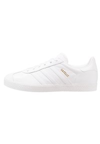 White leather sneaker with three textured stripes and raised sole. Gold "Gazelle" logo on the side. Smooth finish with a classic shape.