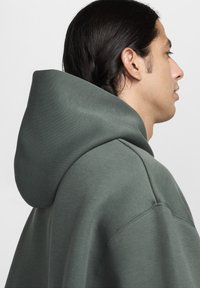 Sweatshirt com capuz em tecido verde escuro, apresentando um corte descontraído, textura suave e costura visível ao longo das costuras.