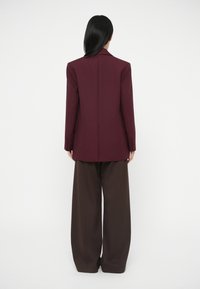 Viininpunainen bleiseri, jossa on jämäkkä istuvuus, yksirivinen malli, terävät kaulukset ja napit, yhdistettynä ruskeisiin leveälahkeisiin housuihin.