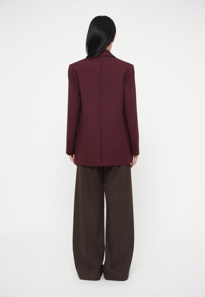 Blazer bordeaux con vestibilità strutturata, design monopetto, revers affilati e dettagli con bottoni, abbinato a pantaloni marroni a gamba larga.