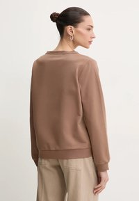 Felpa marrone con collo a giro, polsini e orlo a costine. Tessuto dalla texture liscia, vestibilità rilassata e design minimalista.