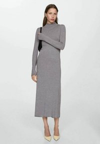 Robe grise à manches longues, avec un col haut et une coupe ajustée. Dotée d'une texture tricot douce, elle atteint le mollet et se marie avec des talons clairs.