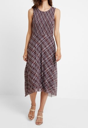 Bruine geruite mouwloze jurk met een aangesloten bovenstuk en uitlopende rok, gemaakt van een getextureerde stof en mid-kuit lengte. Draagt lichte sandalen.