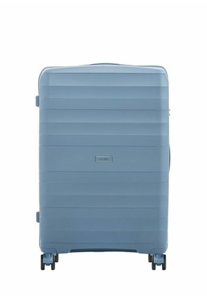 Jasnoniebieska twarda walizka z poziomymi żebrowaniami, cztery czarne podwójne kółka obrotowe i mała prostokątna przednia etykieta z logo.