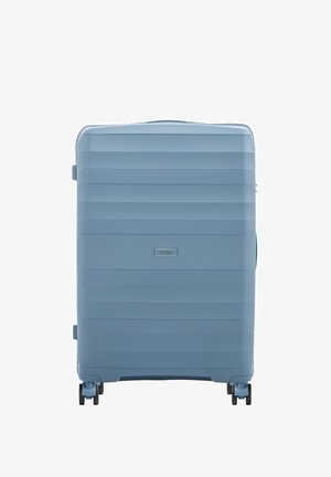 Jasnoniebieska twarda walizka z poziomymi żebrowaniami, cztery czarne podwójne kółka obrotowe i mała prostokątna przednia etykieta z logo.