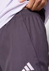 Γκρι αθλητικές βερμούδες με ελαστική μέση, διαθέτουν πλαϊνή τσέπη και λευκές διακοσμητικές λεπτομέρειες με λογότυπο κοντά στο τελείωμα. Το ύφασμα έχει ομαλή υφή.