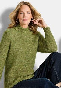 Grüner Strickpullover mit hohem Kragen, strukturiertem Stoff und gerippten Bündchen. Kombiniert mit dunklen Jeans, die eine lockere Passform bieten.