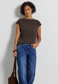 Blouse marron à manches courtes avec une coupe décontractée, associée à un jean large bleu. La blouse présente une texture lisse et un design simple.