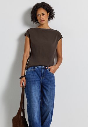 Blouse marron à manches courtes avec une coupe décontractée, associée à un jean large bleu. La blouse présente une texture lisse et un design simple.