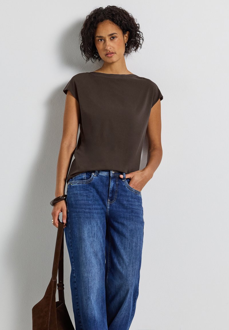 Blouse marron à manches courtes avec une coupe décontractée, associée à un jean large bleu. La blouse présente une texture lisse et un design simple.