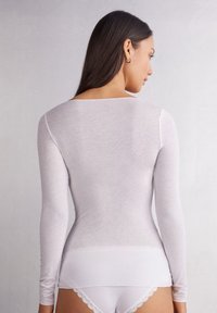 Haut à manches longues blanc en tissu doux et léger. Présente un décolleté en scoop et une coupe ajustée, associé à des culottes blanches avec des accents en dentelle.