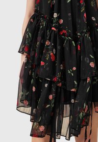 Schwarzes plissiertes Kleid mit floralen Motiven in Rot, Pink und Weiß. Zu sehen sind Rüschenschichten und ein elastisches Taillendetail.