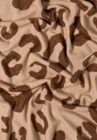 Løveplet stof med en blød beige baggrund og mørkebrun, uregelmæssige pletter. Materialet ser tekstureret og let krøllet ud.