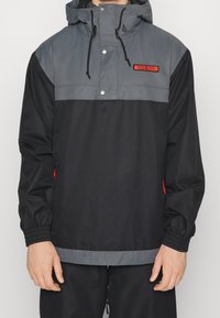 Mustavalkoinen huppari, jossa on puoli-vetoketju, elastiset hihansuut ja punainen logopatch rintamuksessa. Varustettu sivutaskuilla.