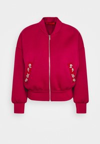 Fuksjowa kurtka bombowca z zamkiem z przodu, oversize'owymi rękawami i zdobionymi kamieniami akcentami kwiatowymi na kieszeniach; wykonana z miękkiego, teksturowanego materiału.