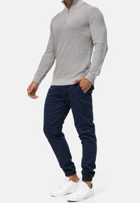 Lichtgrijze ribgebreide trui met een ritskraag, gecombineerd met donkerblauwe taps toelopende joggers en witte sneakers. Nette textuur, casual pasvorm.