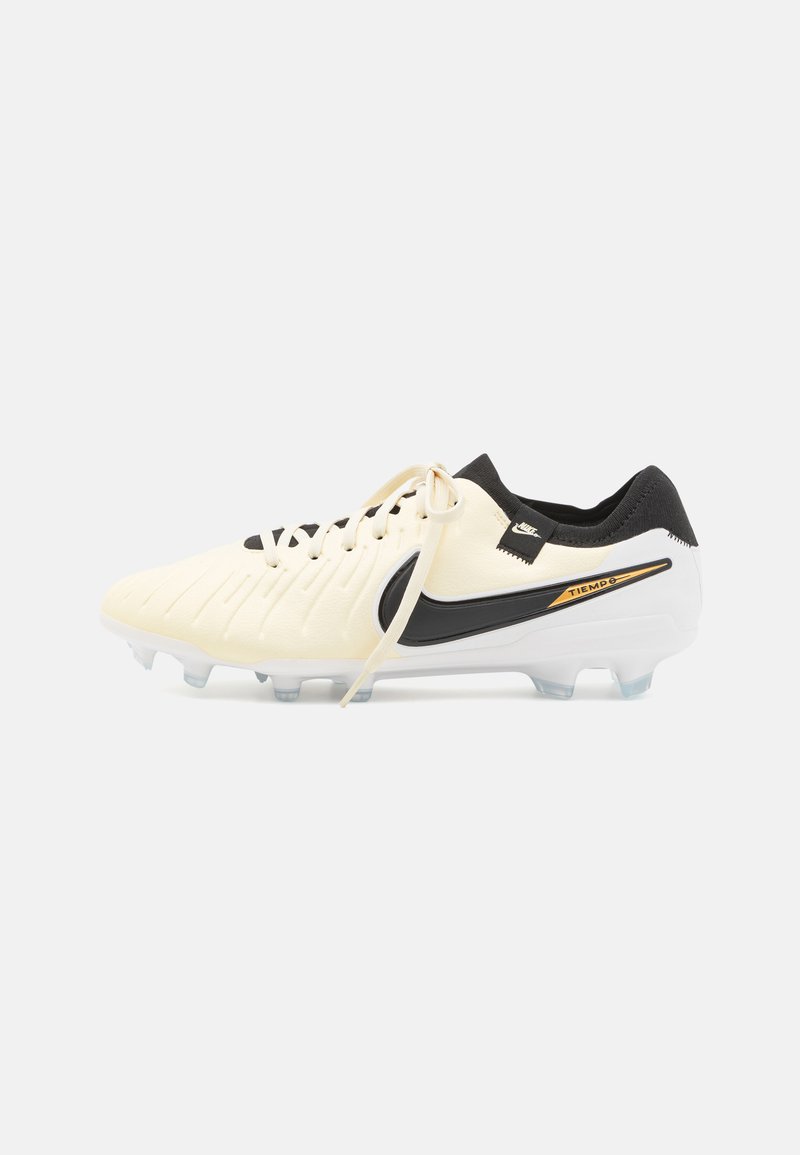Nike Tiempo jalkapallokengät vaaleassa värissä, mustalla swoosh-logolla ja koristeilla. Kenkien pinta on teksturoitu ja niissä on valkoinen pohja, jossa on läpinäkyvät nappulat.