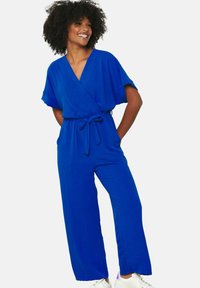 Kobaltovo modrý overal s prekrývajúcim predným dielom, krátkymi rukávmi a opaskom na stiahnutie. Široké nohavice vytvárajú uvoľnený siluet. Hladká textúra látky.