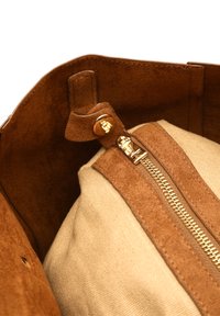 Brauner Wildleder-Innenraum der Tasche mit einem beige Stofffutter und einem Reißverschluss in Goldoptik. Verfügt über einen Druckknopfverschluss und weiche, strukturierte Oberflächen.