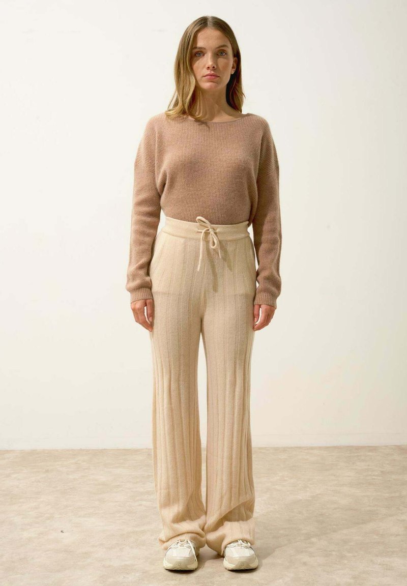 Beige pletený svetr s širokými rukávy v kombinaci s krémovými širokými kalhotami s žebrováním a světlými teniskami. Jednoduchý design s jemnými texturami a tóny.