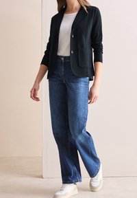 Černé sako se dvěma knoflíky, přední kapsou, nošené přes bílou košili; kombinované s širokými modrými džíny a bílými teniskami.