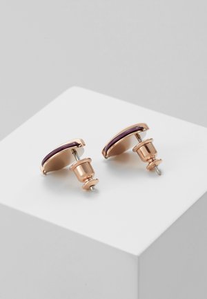 Paire de boucles d'oreilles clous rondes en métal or rose avec accents en émail violet, posées sur une surface blanche, vue en angle.