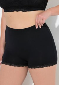 Shorts di cotone neri con una texture liscia e un bordo decorativo in pizzo all'orlo. Presentano una vita alta e un design aderente.