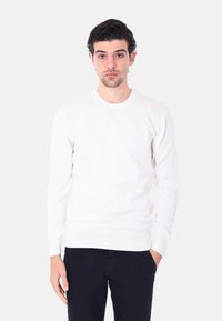 Maglione lungo bianco a maniche lunghe con scollo a girocollo e polsini a costine. Il tessuto appare liscio e leggero, adatto per essere indossato a strati.