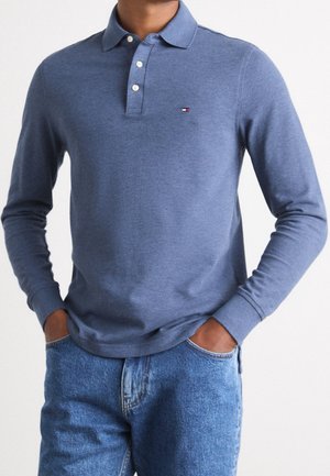 Polo à manches longues en mélange de coton bleu chiné, avec une patte de boutonnage à trois boutons et un petit logo sur la poitrine. Associé à un jean bleu.