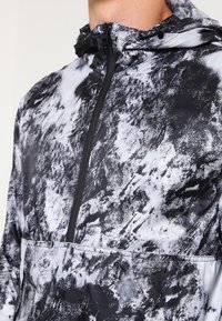 Czarna i biała kurtka przeciwwiatrowa z kapturem, z teksturowanym, abstrakcyjnym wzorem, przednim suwakiem i bezszwowym dołem.