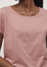 Short-sleeve pink cotton t-shirt with a wide neckline and smooth texture. Stitching detail along the neckline and sleeves.
