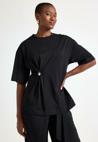 T-shirt nera a maniche corte con dettaglio annodato in vita, realizzata in una morbida miscela di cotone, caratterizzata da una vestibilità comoda e scollo rotondo.