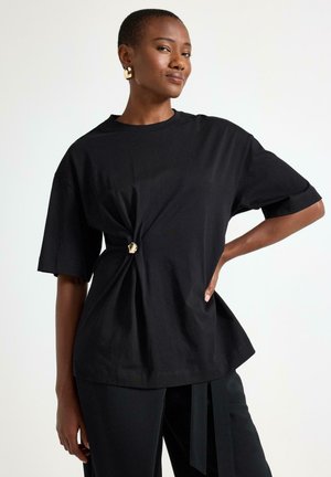 Sort T-shirt med korte ærmer og en knude ved taljen, lavet af en blød bomuldsblanding, med en afslappet pasform og rund halsudskæring.