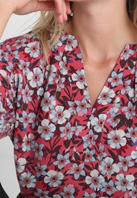 Floral blouse featuring a v-neck design with blue and white flowers on a pink background; lightweight fabric with a smooth texture.