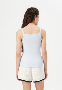 Lys blå ribbestrikket tanktop med tynne stropper, tettsittende design. Kombinert med hvite teksturerte shorts med svart bølget kant langs nederkanten.