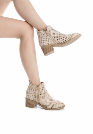 Botas de tobillo beige con cuero perforado, tacón bajo apilado, cremallera lateral y punta redonda. Patrón texturizado notable en la parte superior.
