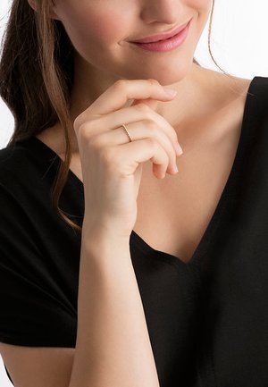 Goldring mit strukturierter Gestaltung, getragen an der Hand eines Models. Das Model trägt ein schwarzes V-Ausschnitt-Top.