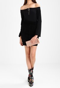 Czarna bluzka bez ramiączek z ozdobnym srebrnym zamkiem, czarna zamszowa mini spódnica, kwiatowe botki za kostkę oraz różowo-złota torebka o fakturze.