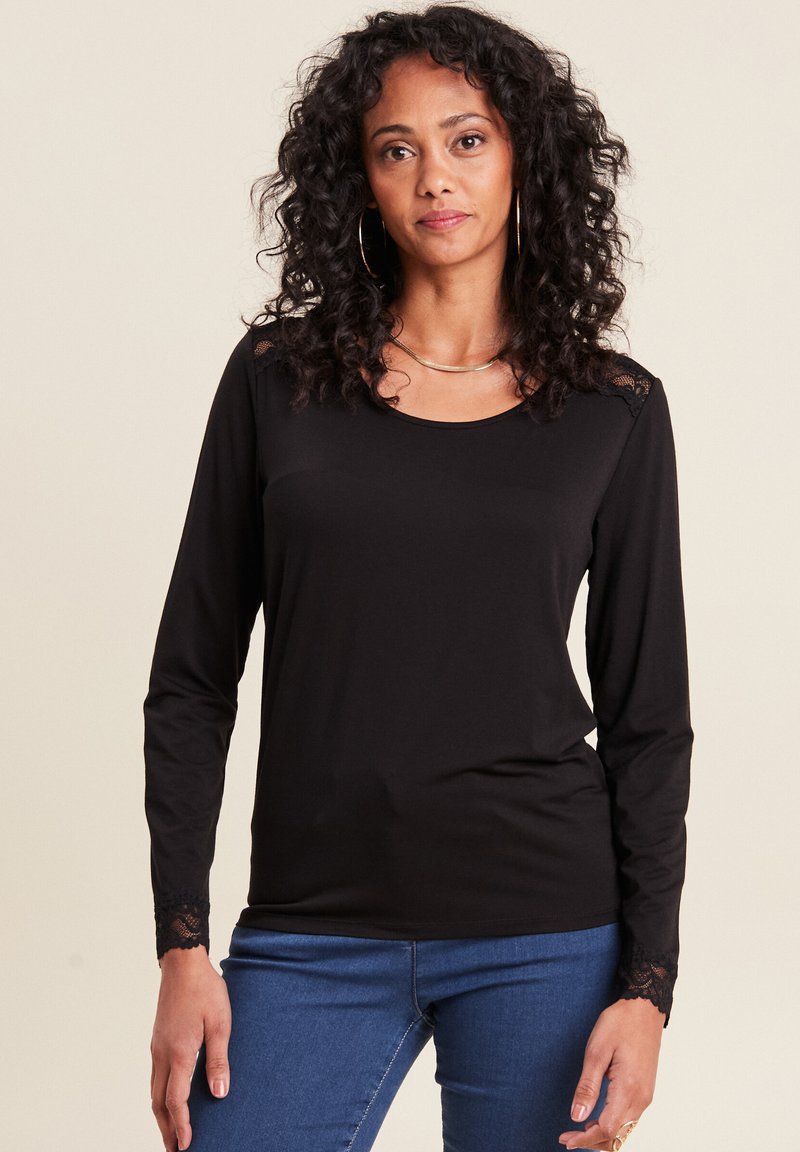 Schwarzes langärmliges Oberteil aus weichem Stoff, mit rundem Halsausschnitt und Spitzenakzenten an den Ärmeln. Kombiniert mit blauen Jeans.