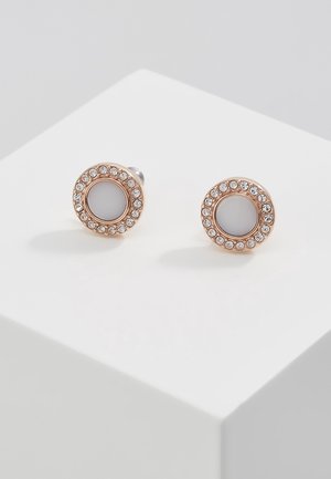 Paire de boucles d'oreilles clous rondes en or rose avec cercles centraux en émail blanc entourés de cristaux clairs, présentées sur un piédestal cube blanc.