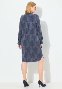 Tummansininen pitkähihaisellinen mekko, jossa on teksturoitu kukkakuosi, sivuaukot ja takana laskos. Yhdistettynä tummiin korkokenkiin.